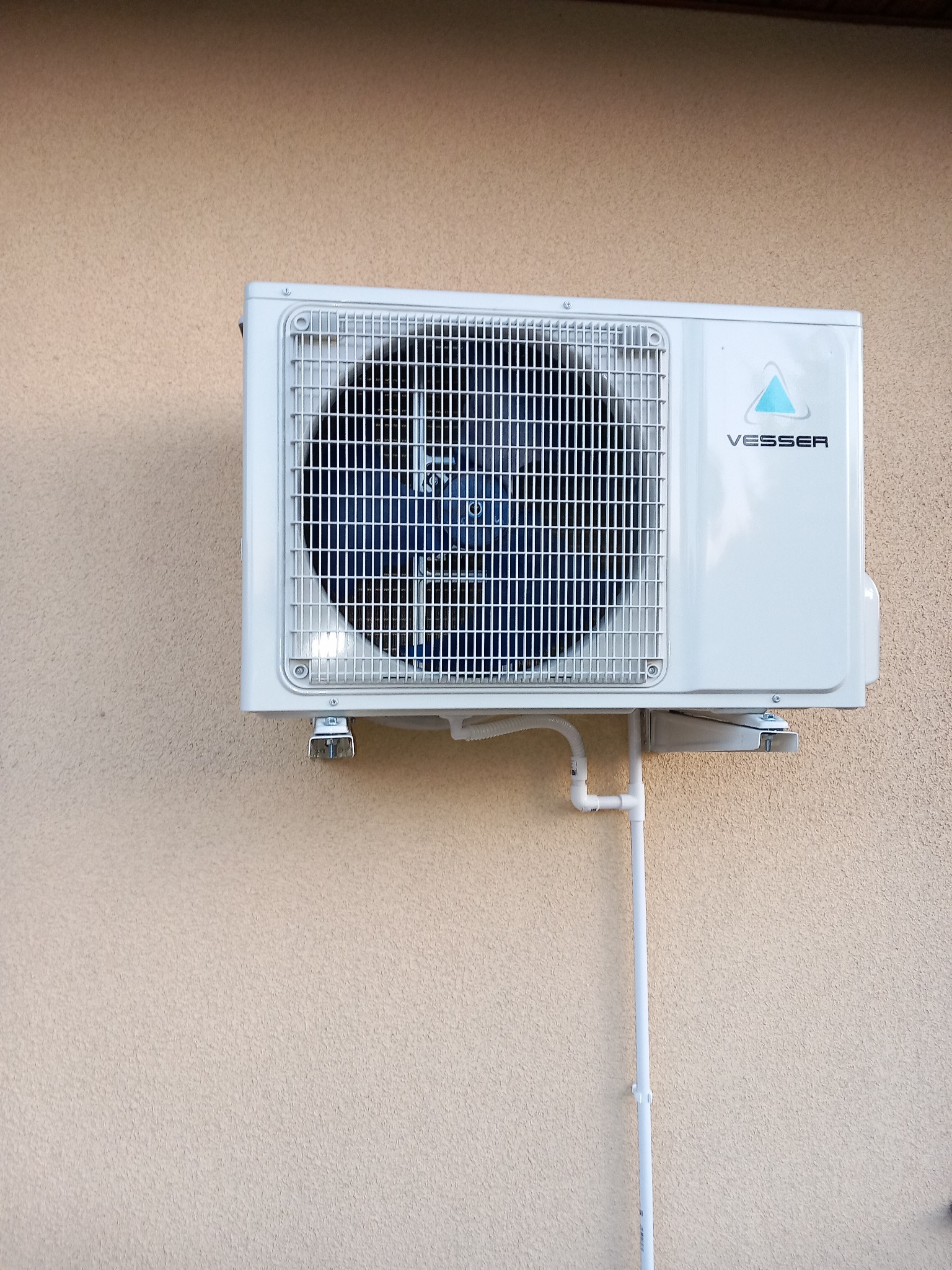 Zewnętrzna jednostka klimatyzacji Vesser zamontowana na ścianie budynku, z widocznymi rurami odprowadzającymi skropliny.