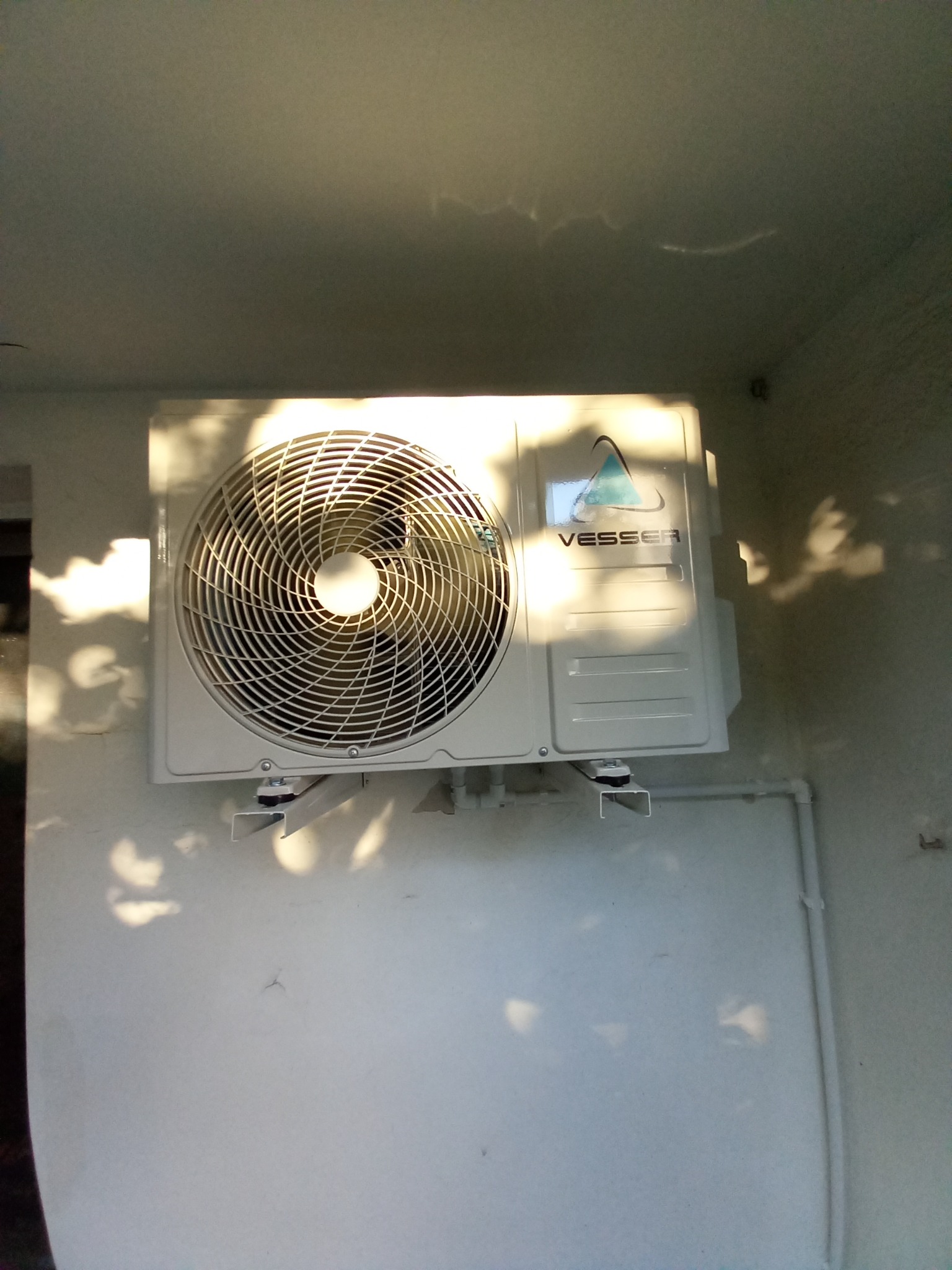 Zamontowana jednostka zewnętrzna klimatyzacji Vesser na jasnej ścianie budynku, oświetlona promieniami słońca, widoczne rury instalacji.