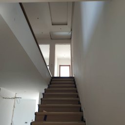 Mixa-Bud - Schody zabezpieczone kartonem i taśmą malarską przed malowaniem ścian w jasnym wnętrzu domu.