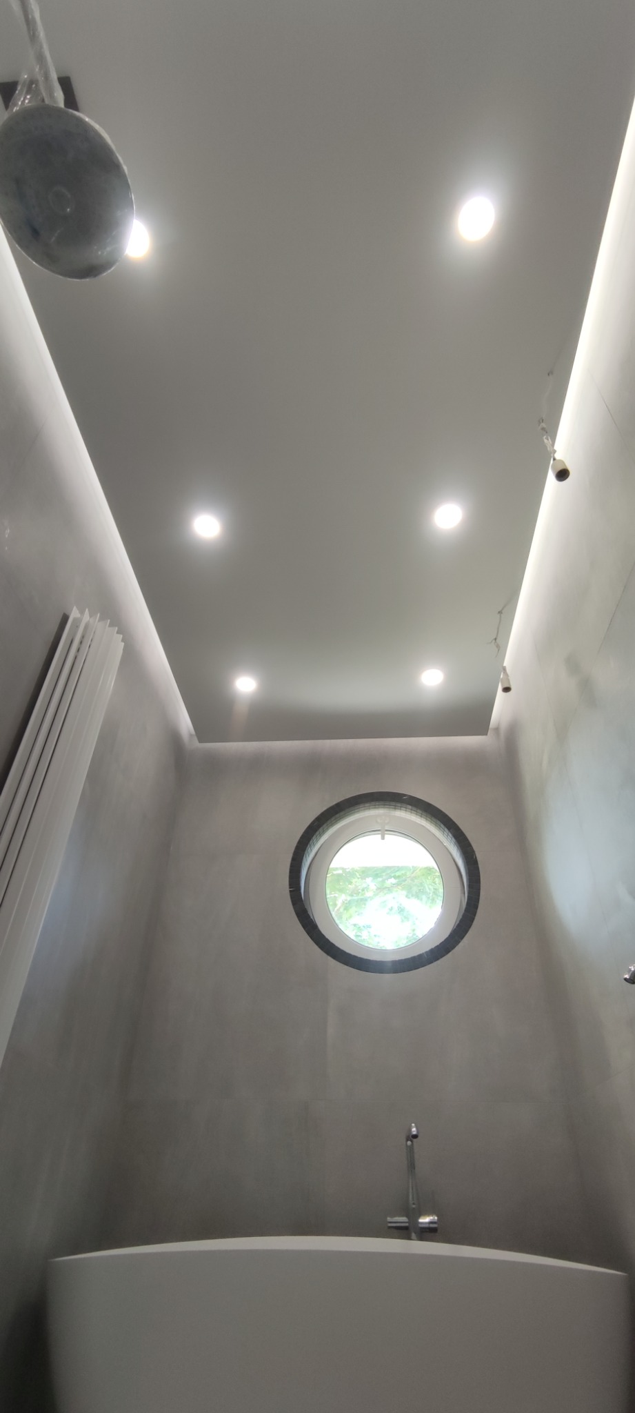 Nowoczesna łazienka z okrągłym oknem, minimalistyczną wanną i szarą, gładką powierzchnią ścian.