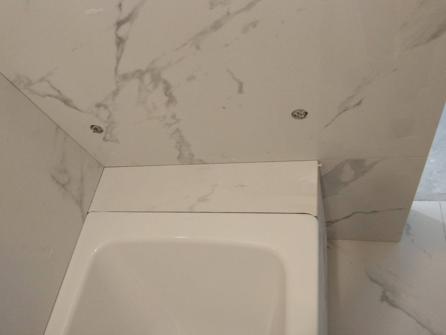 Fragment wykończonej łazienki z wanną obudowaną płytkami imitującymi marmur i punktowym oświetleniem sufitowym.