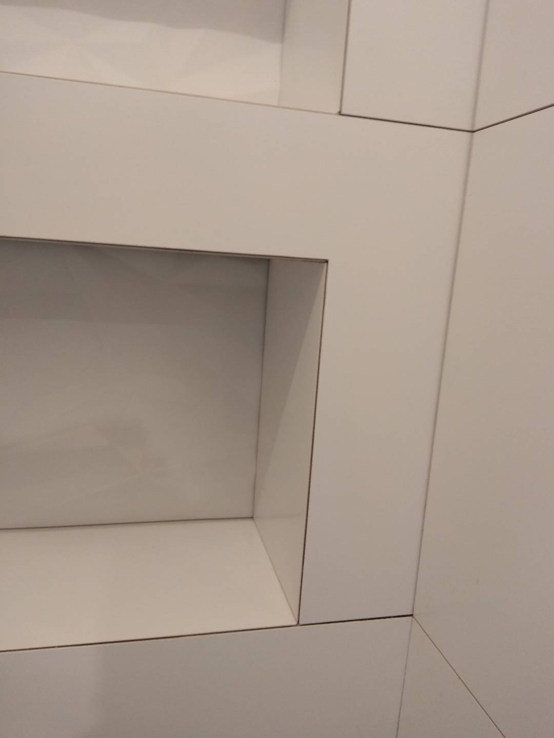 Wnęka w ścianie wykończona białymi płytami, widoczne precyzyjne łączenia i minimalistyczny design.