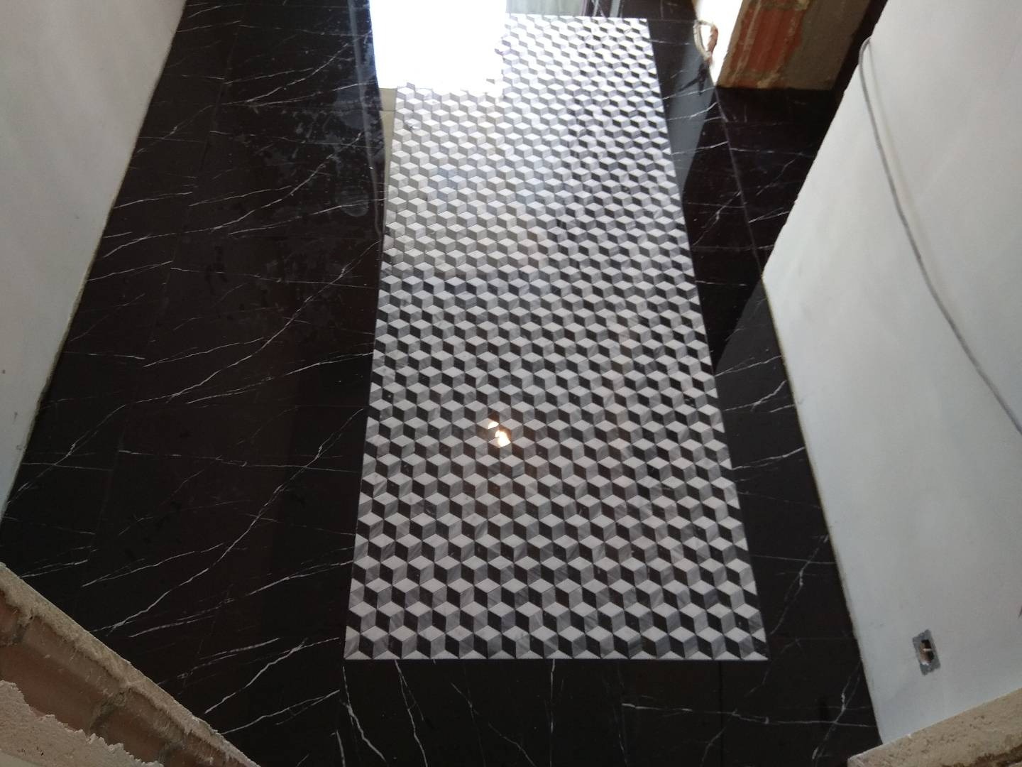 Ułożona podłoga z płytek: czarne płytki imitujące marmur z białymi żyłami po bokach i centralny pas z płytek z geometrycznym wzorem 3D kostek.