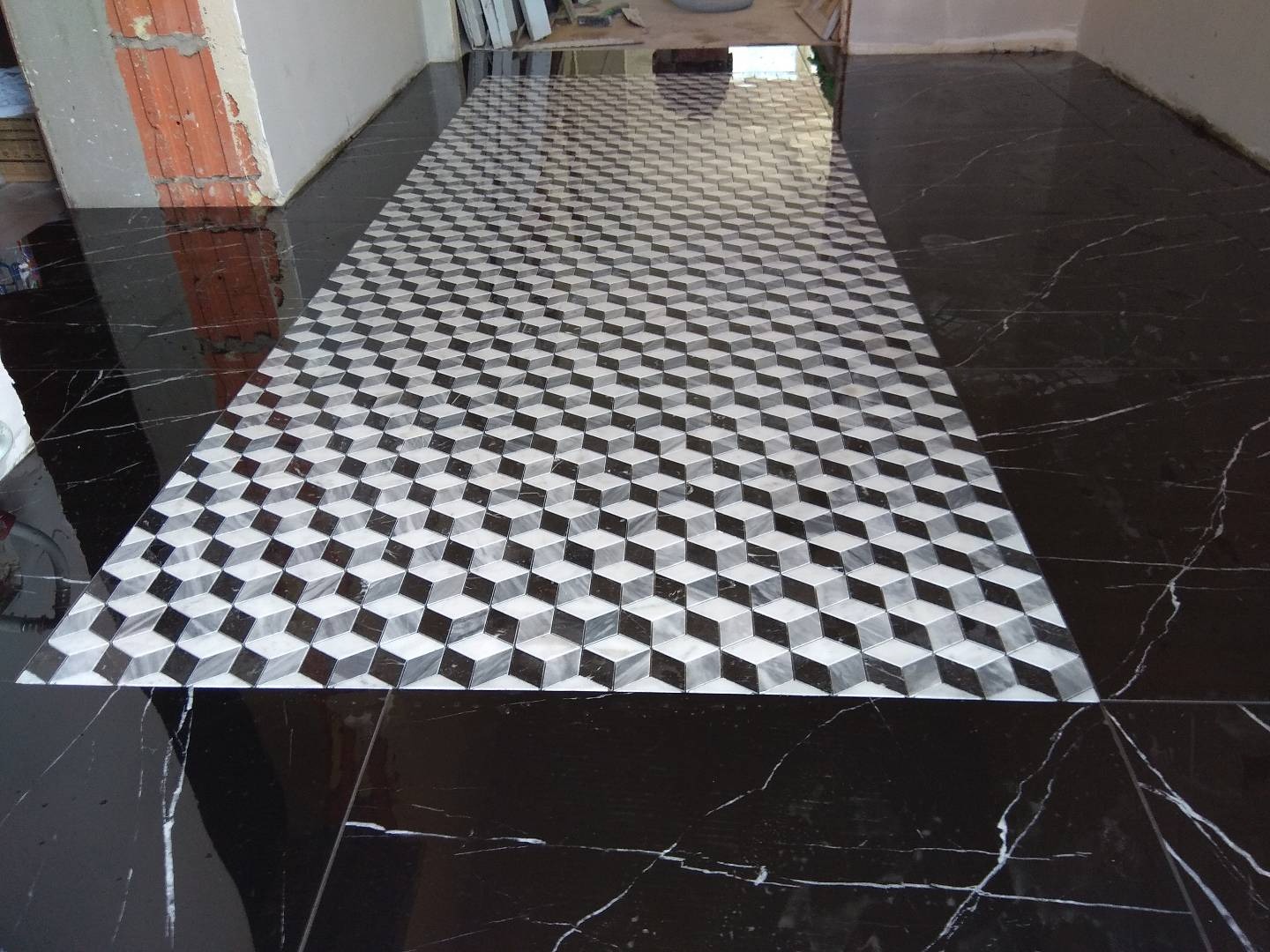 Ukończona podłoga z czarnego marmuru z białym wzorem 3D kostek na środku, widoczne niedokończone ściany po bokach.