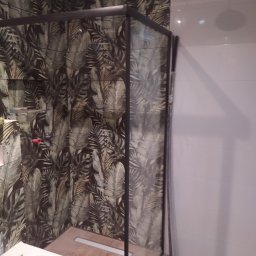 Remonty - Nowoczesna łazienka z kabiną prysznicową typu walk-in z czarnymi profilami, płytkami w tropikalne liście na jednej ścianie i białymi płytkami na pozostałych, oraz toaletą w rogu.