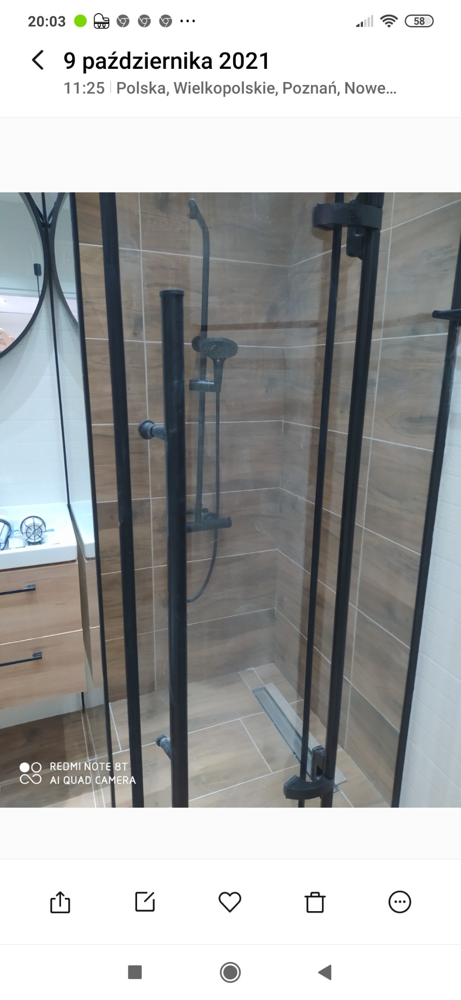 Nowoczesna kabina prysznicowa z czarnymi profilami i armaturą, widoczny odpływ liniowy w podłodze wyłożonej płytkami imitującymi drewno, umywalka z szafką w tle.