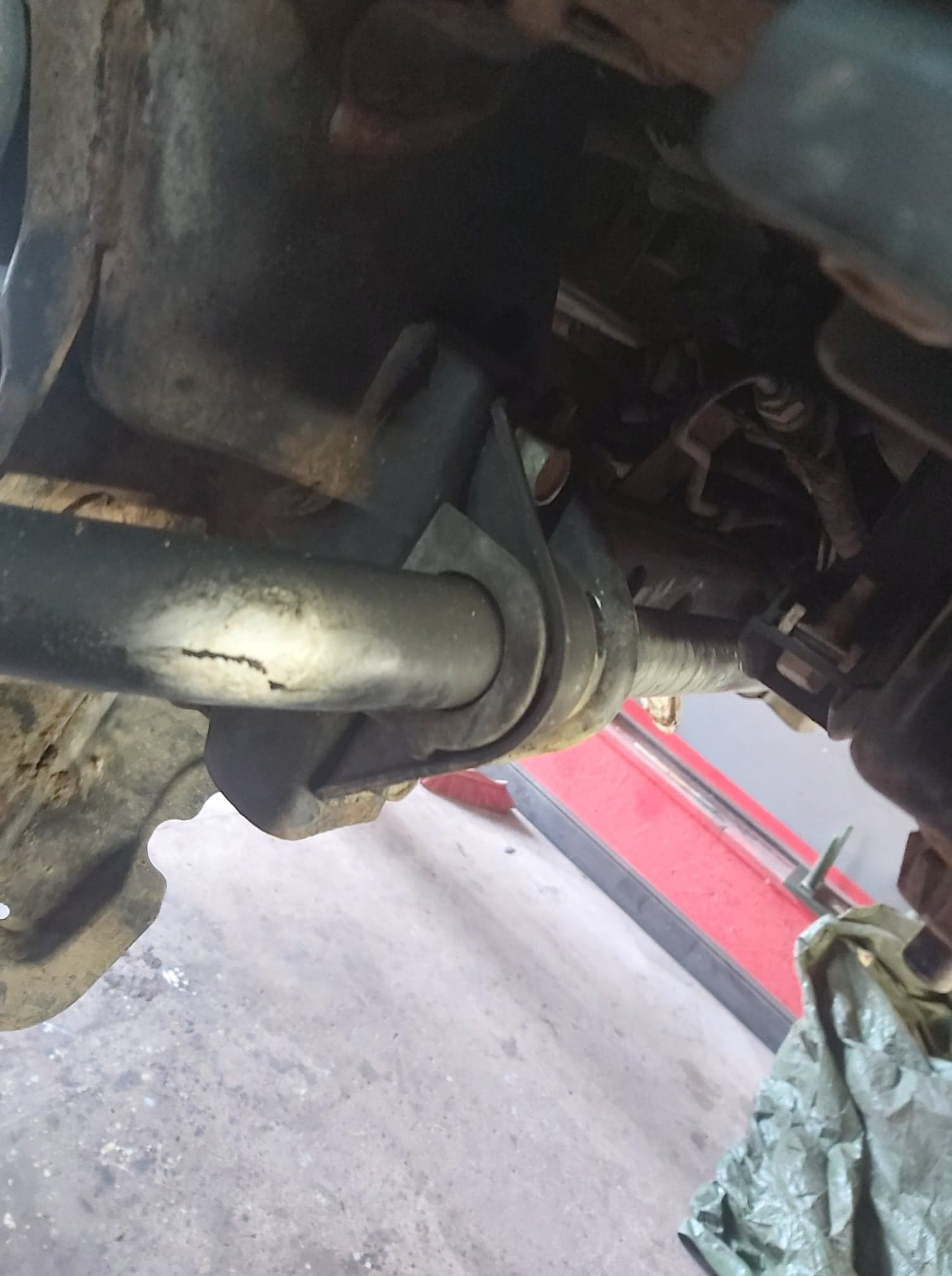 Zawieszenie samochodu z widocznym pęknięciem na stabilizatorze, ujęcie z dołu w warsztacie.