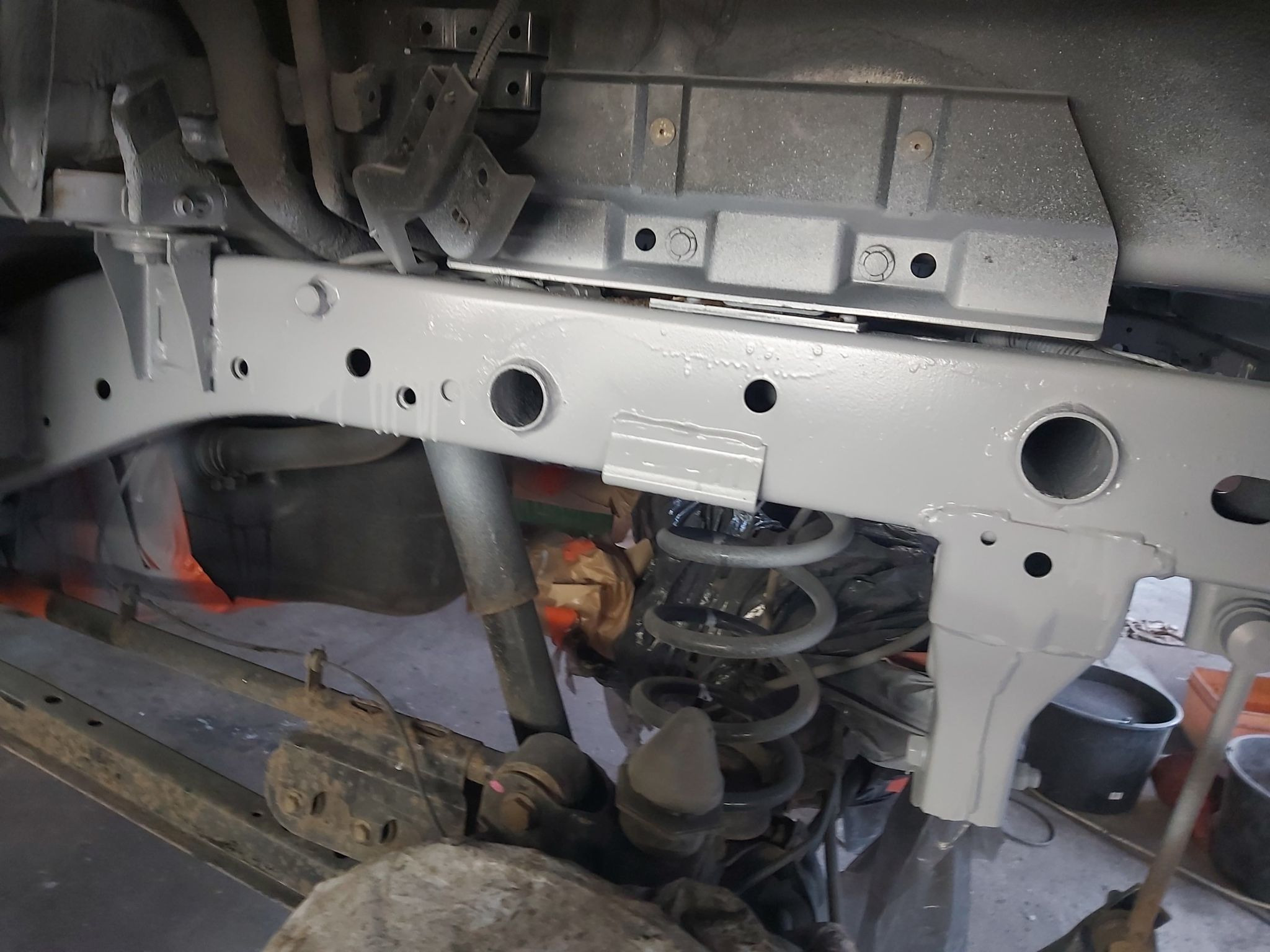 Podwozie samochodu po zabezpieczeniu antykorozyjnym, widoczne elementy zawieszenia pomalowane na szaro. Świeżo nałożona powłoka ochronna z widocznymi śladami po zabezpieczeniu.