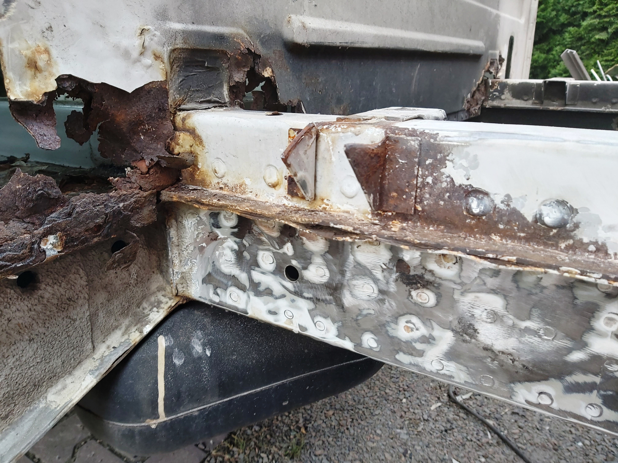 Fragment skorodowanego podwozia samochodu w trakcie naprawy blacharskiej, widoczne ogniska rdzy i obszary z nałożoną szpachlą.