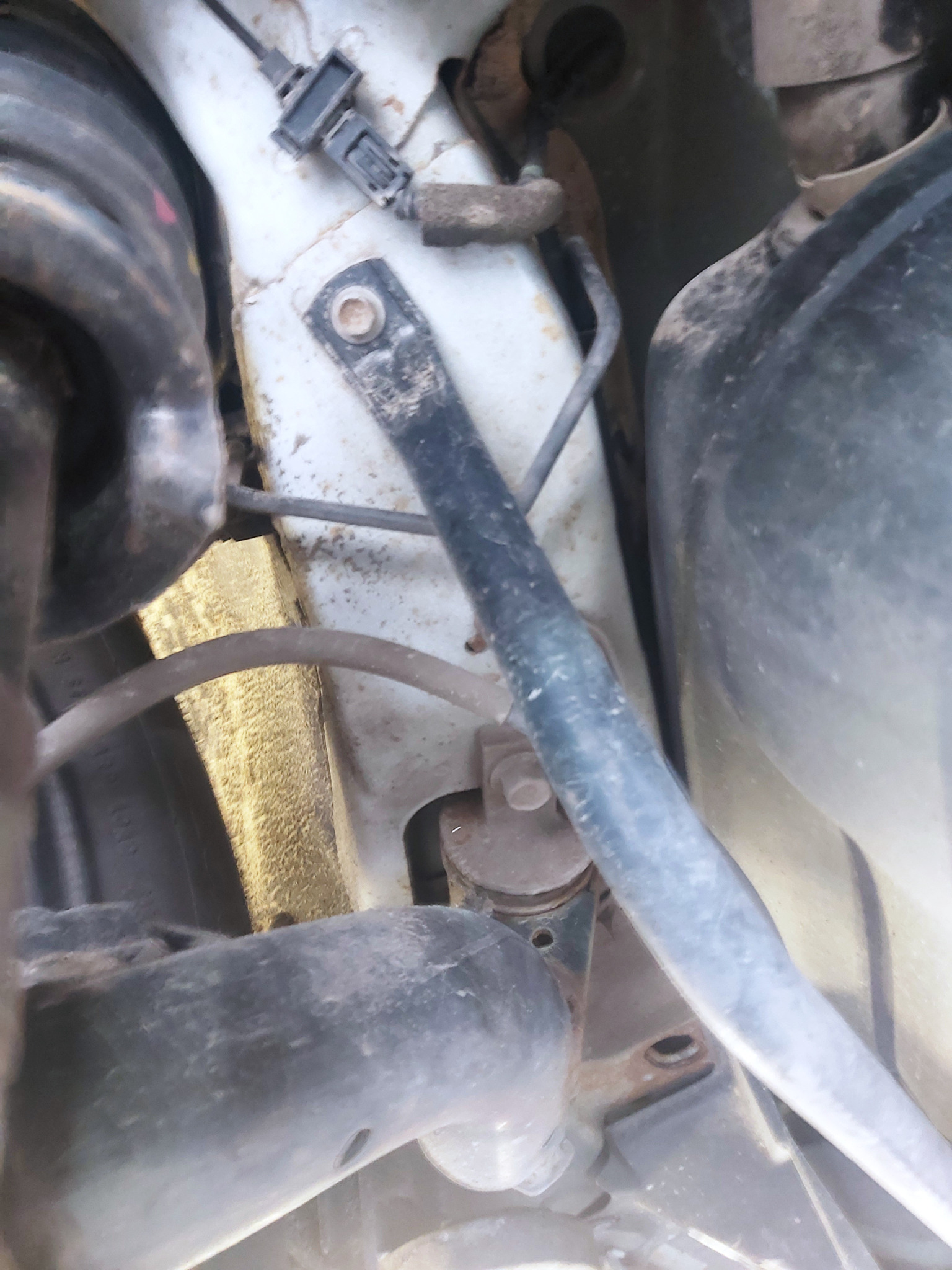 Widok podwozia samochodu z widocznymi elementami zawieszenia, przewodami i złączką elektryczną, wszystko pokryte warstwą kurzu i brudu.