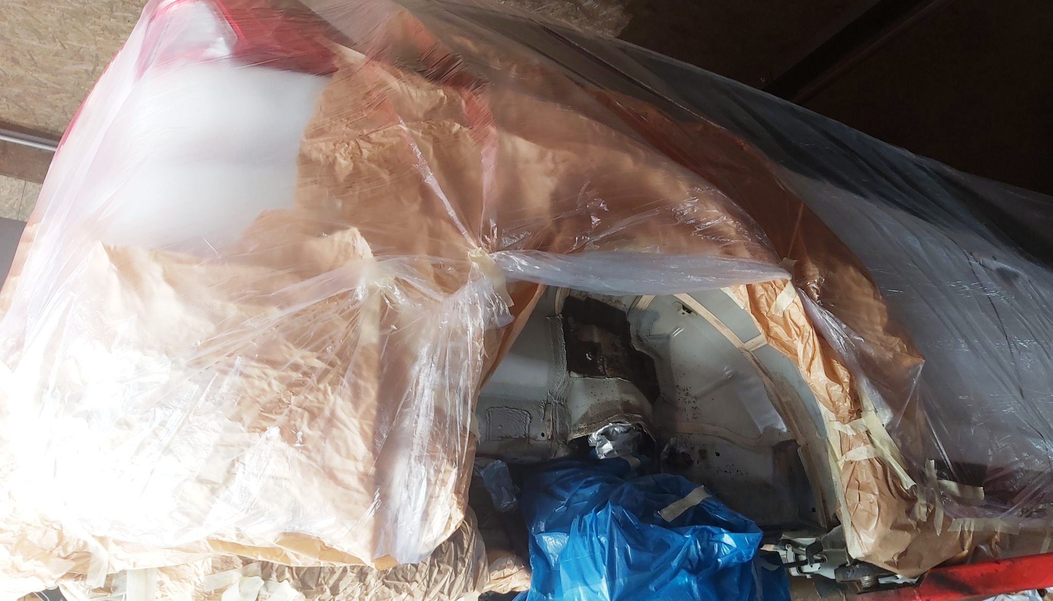 Przygotowanie karoserii samochodu do lakierowania: zabezpieczone elementy papierem i folią, widoczne fragmenty skorodowanej blachy i elementy konstrukcyjne.