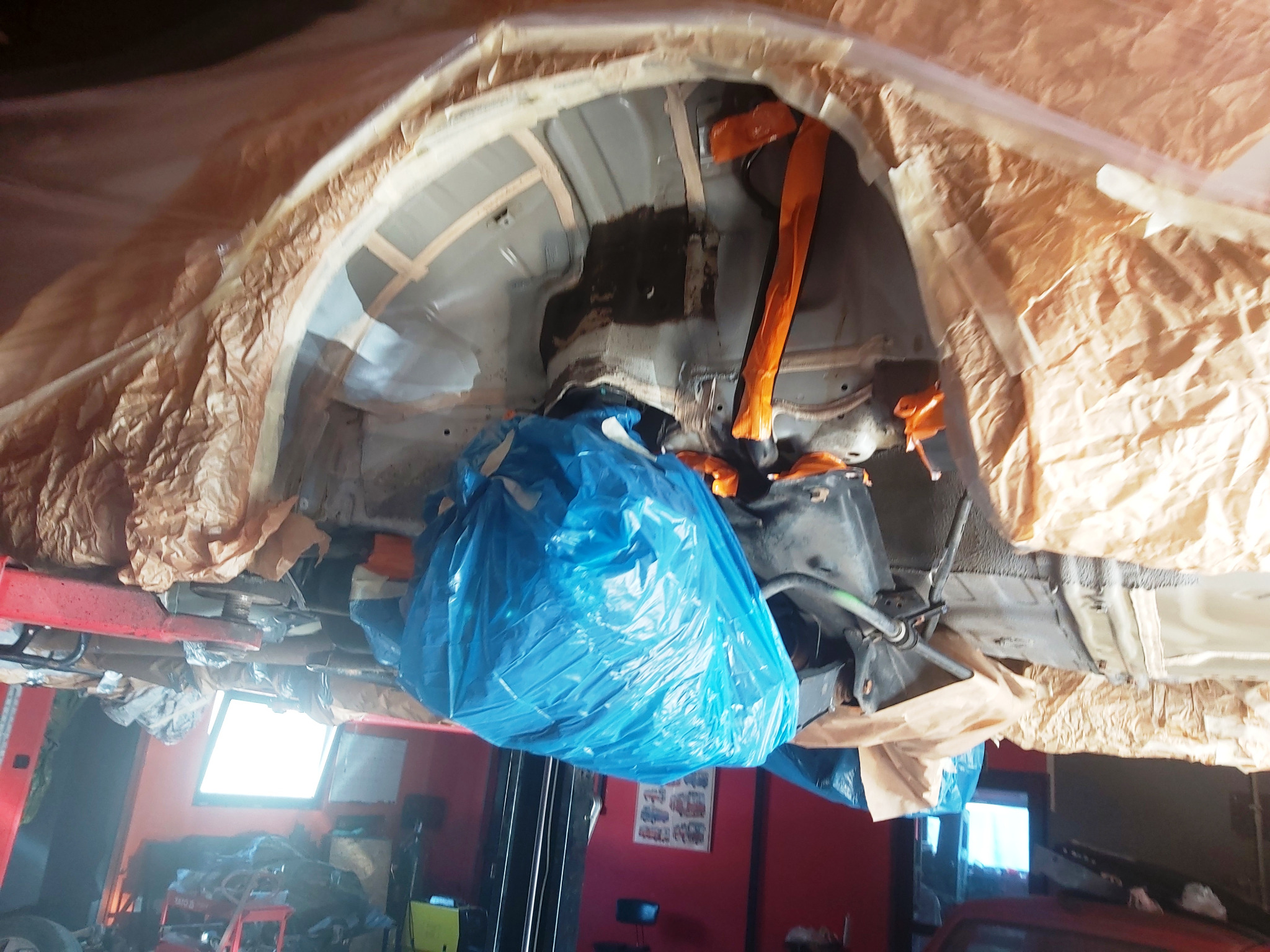 Podwozie samochodu zabezpieczone folią i taśmą przed pracami konserwacyjnymi, widok od dołu z podnośnika.