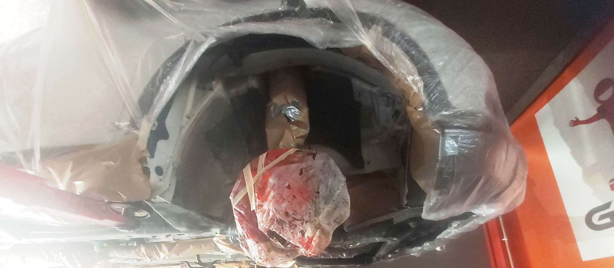 Nowe elementy karoserii samochodowej, owinięte folią i papierem, przygotowane do montażu, widoczne w warsztacie.