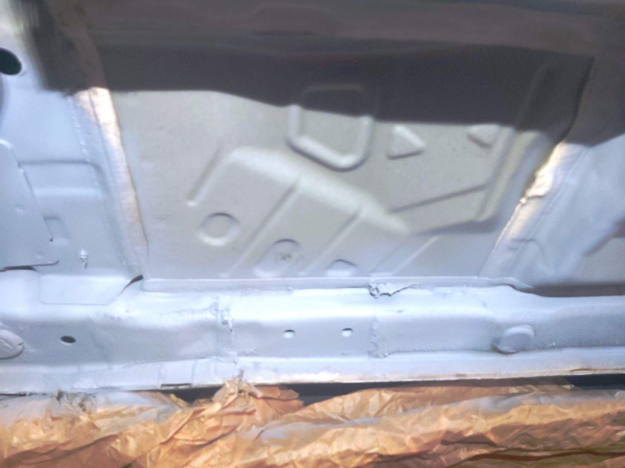 Spód samochodu po nałożeniu warstwy antykorozyjnej, widoczne spawy i zabezpieczone folią elementy.