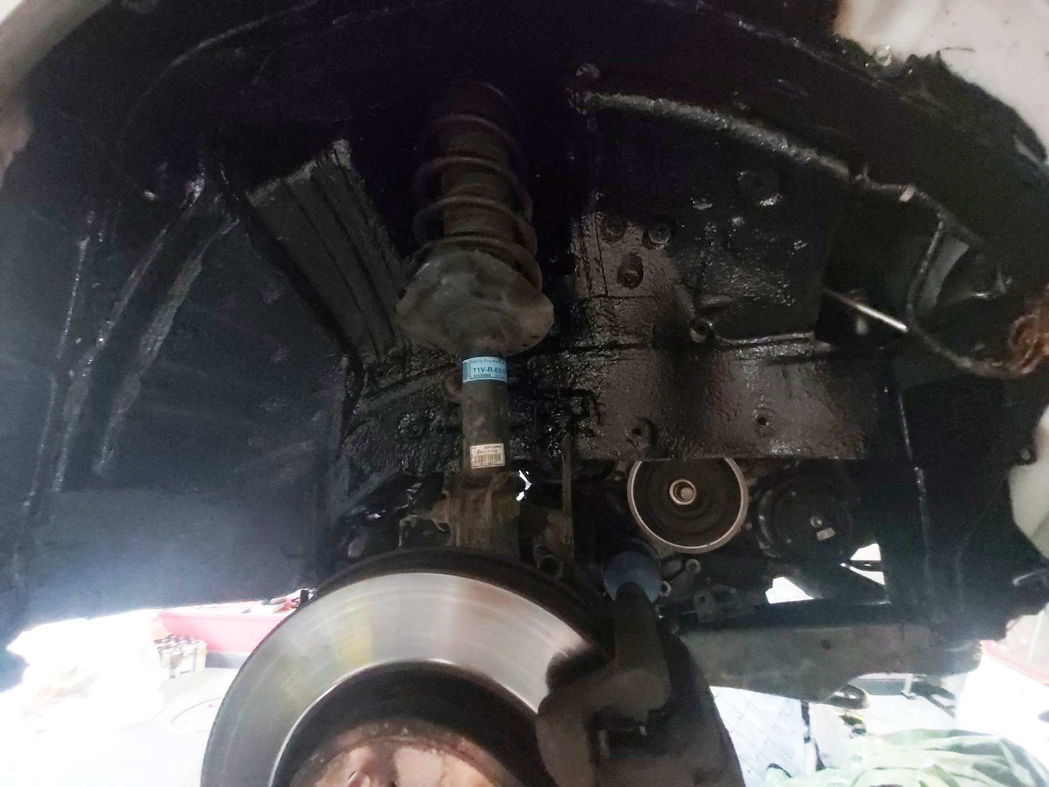 Podwozie samochodu po nałożeniu czarnej powłoki antykorozyjnej, widoczny amortyzator, tarcza hamulcowa i elementy zawieszenia.