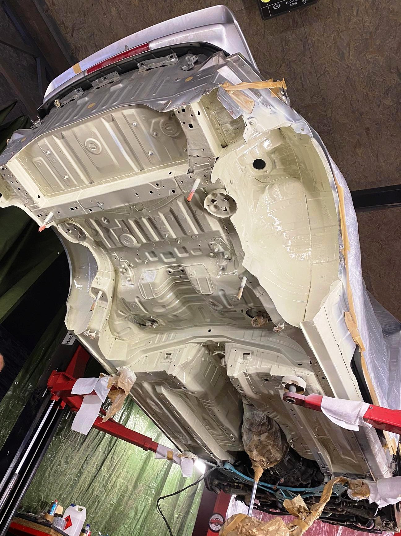 Podwozie samochodu po nałożeniu warstwy antykorozyjnej, widoczne zabezpieczenia elementów i podnośnik warsztatowy.