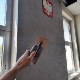 LaDeKo - Nakładanie dekoracyjnego tynku w odcieniach szarości na ścianę w pomieszczeniu biurowym, widoczny herb Polski i fragment okna.