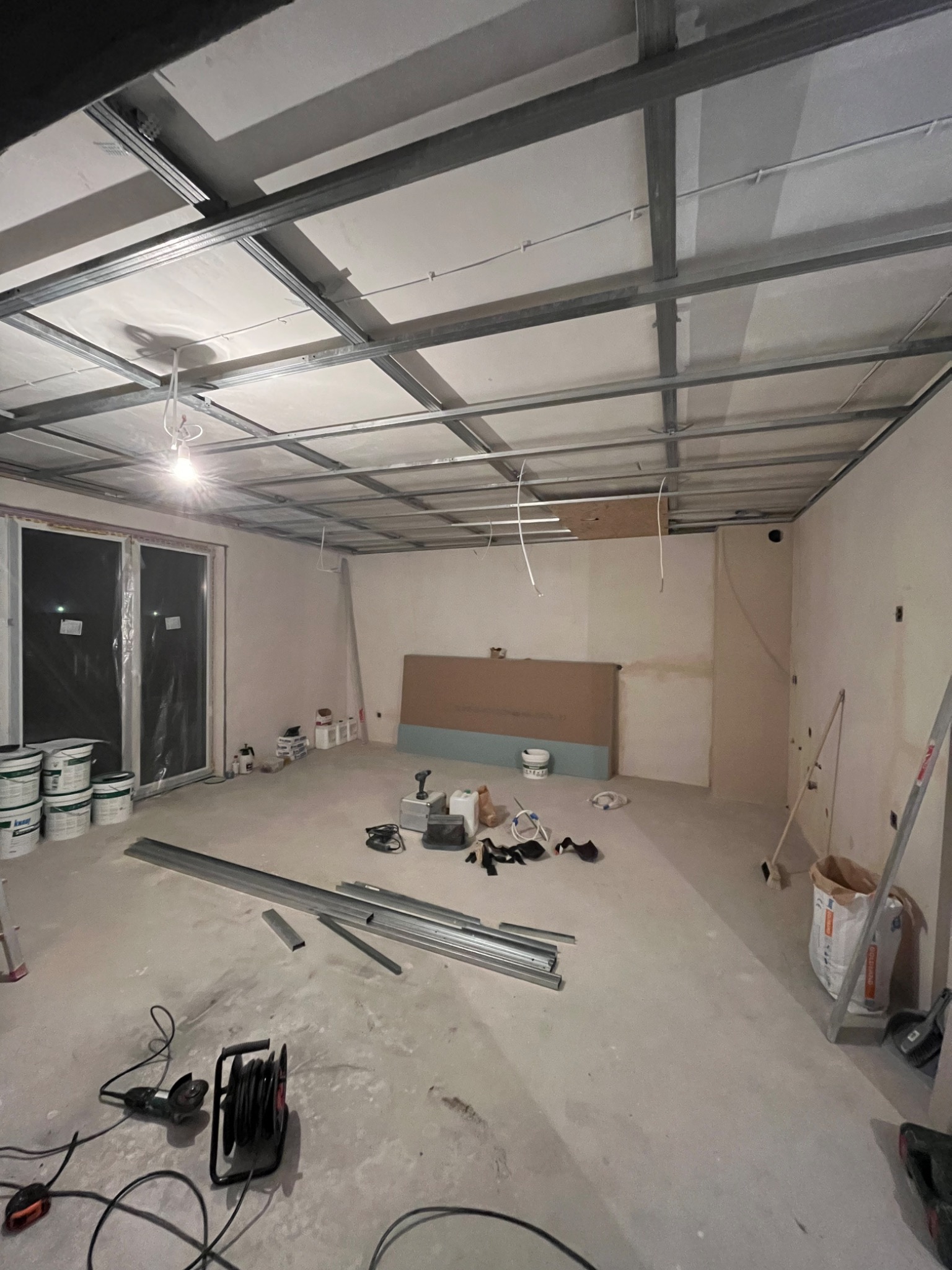 Wnętrze w trakcie montażu sufitu podwieszanego z płyt kartonowo-gipsowych, widoczne profile metalowe, płyty, narzędzia oraz materiały budowlane.