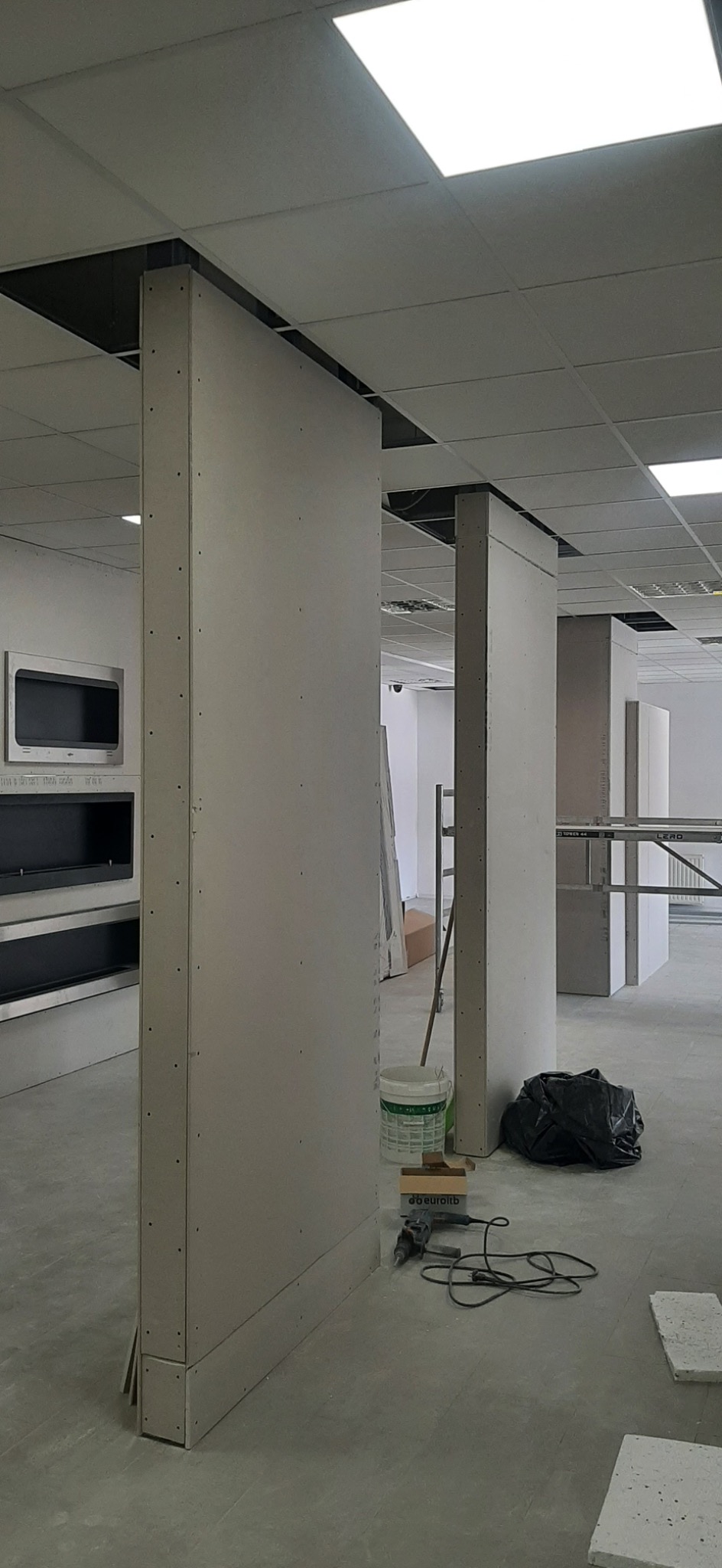 Montaż szkieletu ścianki działowej z płyty kartonowo-gipsowej w biurze, widoczne profile, płyty, narzędzia i wiadro farby.