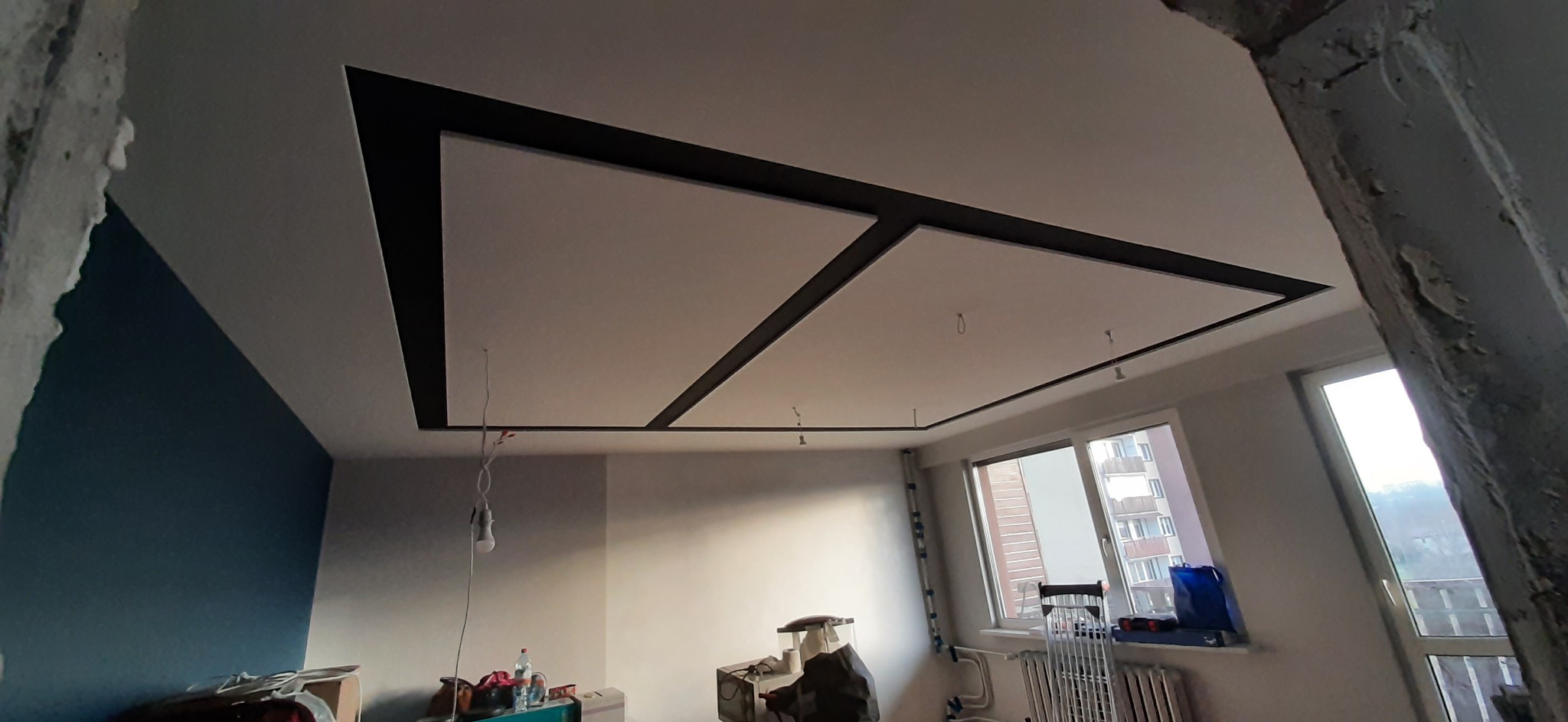 Wykończony sufit z płyt kartonowo-gipsowych z czarnymi listwami dekoracyjnymi, widok z dołu, pokój w trakcie remontu.