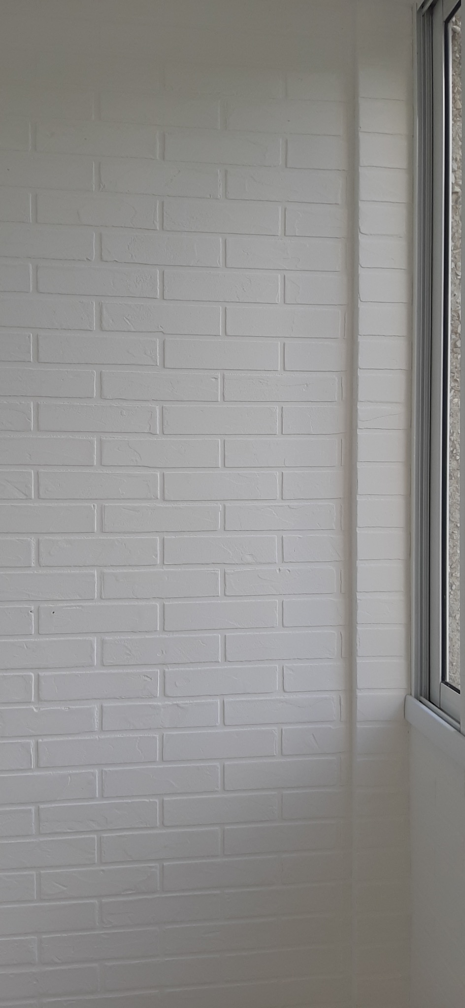 Ściana z białej cegły dekoracyjnej w rogu pokoju, widoczne okno z szarą ramą.