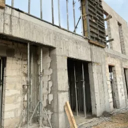 Surowy stan budowy biurowca w województwie lubelskim: ściany z betonu komórkowego w trakcie wznoszenia, stalowe podpory i szalunki widoczne, przygotowane otwory okienne.