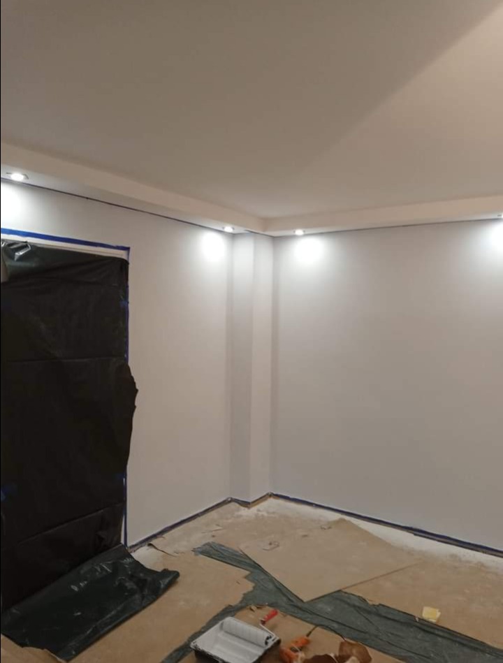 Pokój w trakcie odświeżania: świeżo pomalowane ściany w jasnym odcieniu, zabezpieczone folią i taśmą malarską, widoczny wałek i kuweta malarska na podłodze.