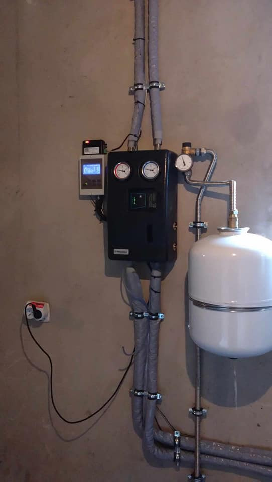 Zamontowana instalacja z czarnym panelem sterującym, białym zbiornikiem i izolowanymi rurami wewnątrz budynku.