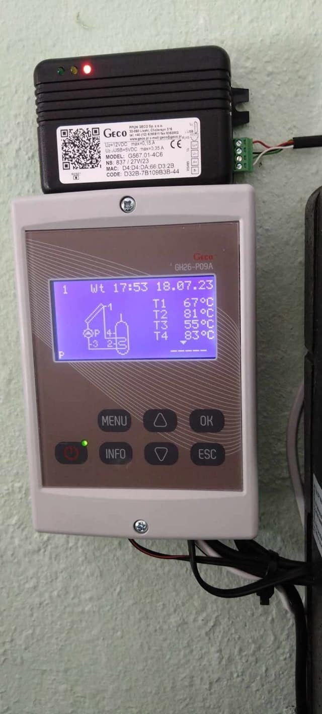 Panel sterowania systemem solarnym Geco GH26-P09A z wyświetlanymi temperaturami T1-T4 oraz schematem instalacji, zamontowany obok czarnej skrzynki z diodami LED i kodem QR.