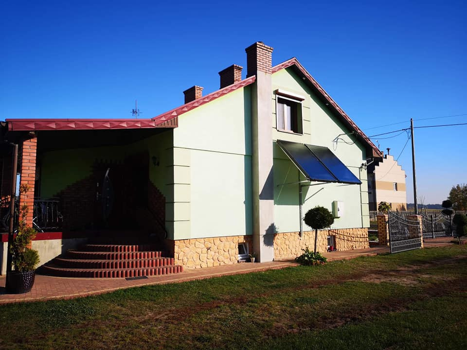 Dom jednorodzinny z zamontowanymi dwoma panelami słonecznymi na elewacji, widoczne okno i zielony trawnik.