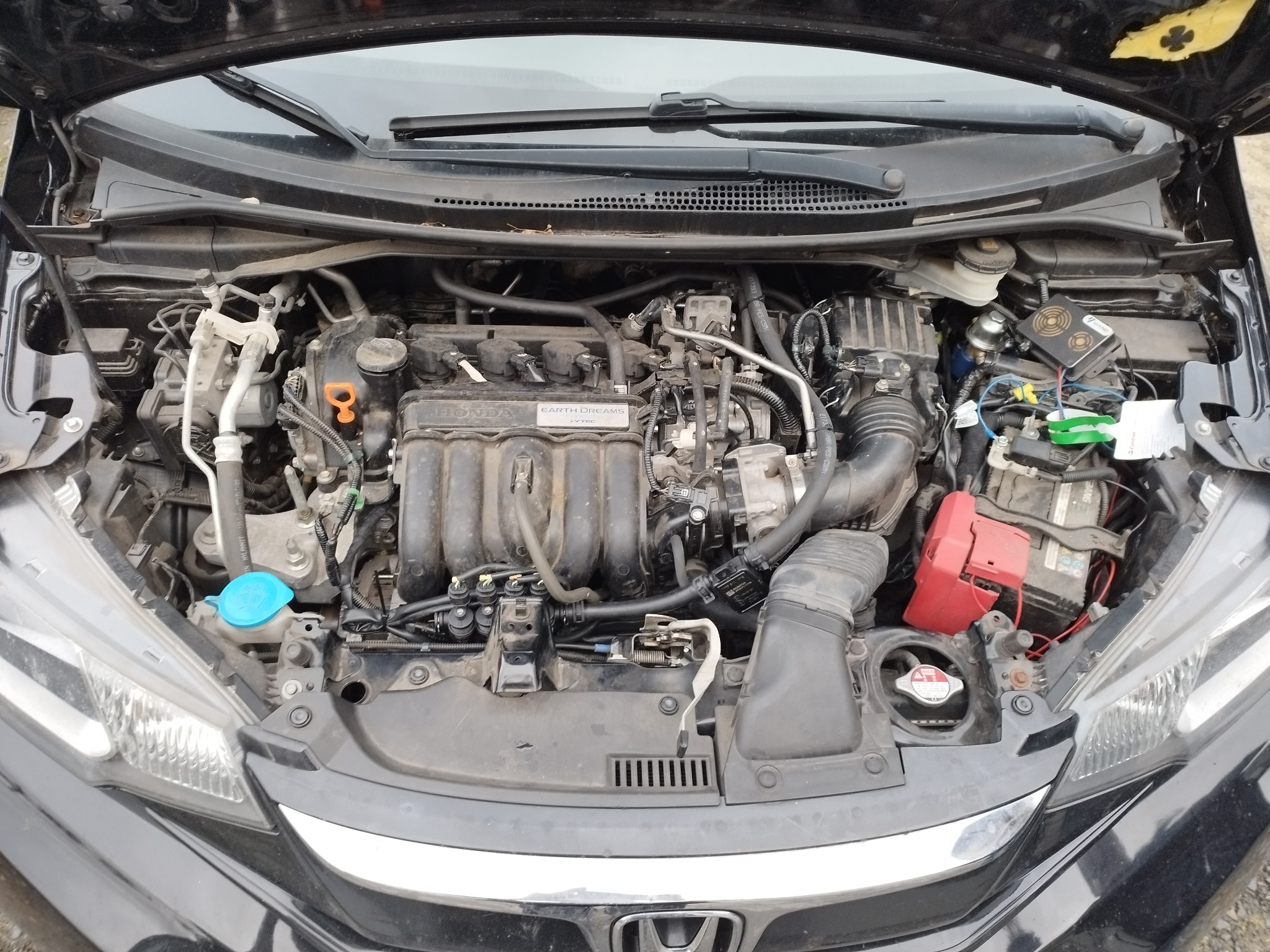 Otwarta maska czarnej Hondy z widocznym silnikiem i elementami instalacji gazowej, w tym wtryskiwacze gazu i reduktor, z widoczną tabliczką znamionową silnika z napisem 'HONDA EARTH DREAMS i-VTEC'.