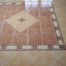 Wykończona podłoga z brązowych i beżowych płytek w aranżacji kwadratu z dekoracyjną ramką, ułożona w Grzybnie.