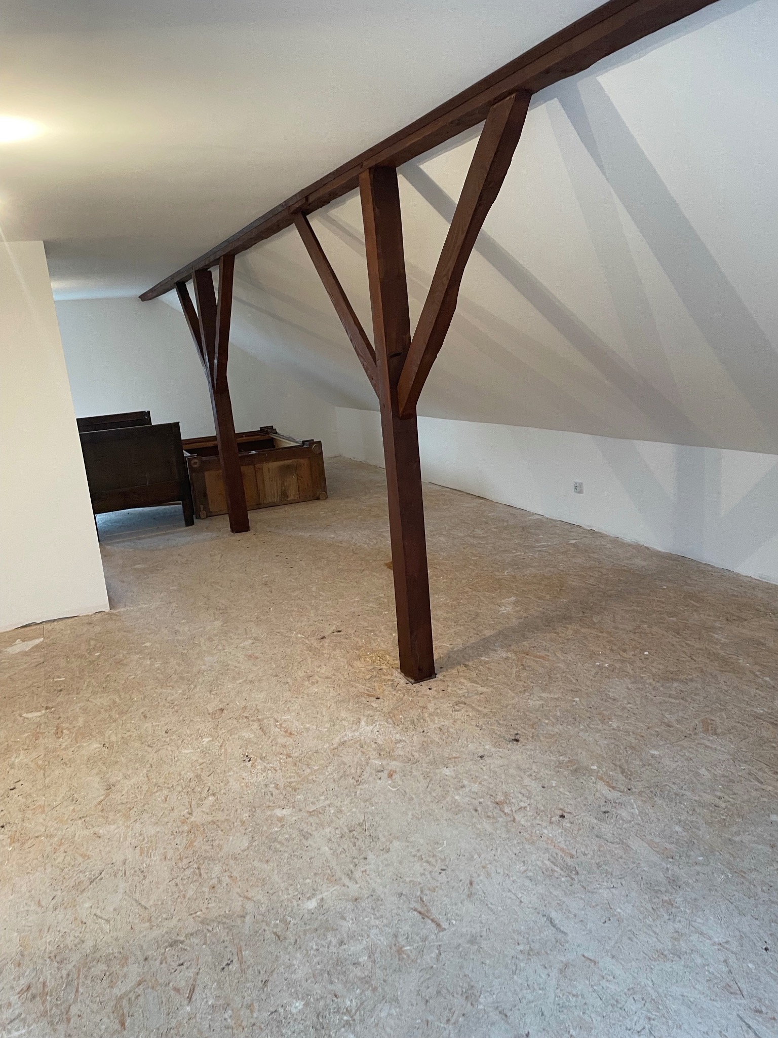 Poddasze z drewnianą konstrukcją nośną i podłogą z płyt OSB, przygotowane do dalszych prac wykończeniowych, widoczne meble częściowo zakryte.