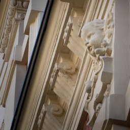 Busy Bee Sp. zo.o. - Detal fasady budynku z dekoracyjnym fryzem i rzeźbą głowy aniołka, widok z dołu, oświetlenie boczne.