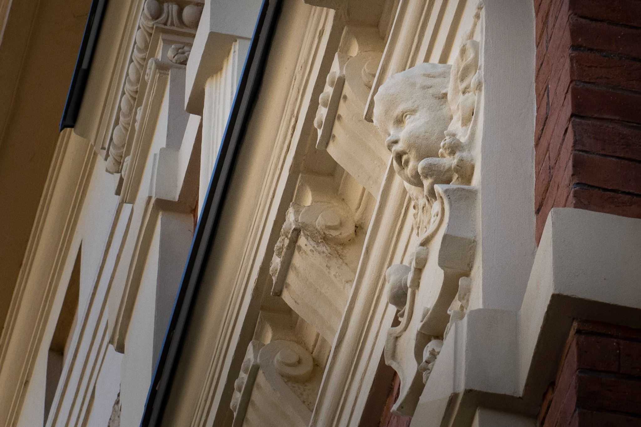 Detal fasady budynku z dekoracyjnym fryzem i rzeźbą głowy aniołka, widok z dołu, oświetlenie boczne.