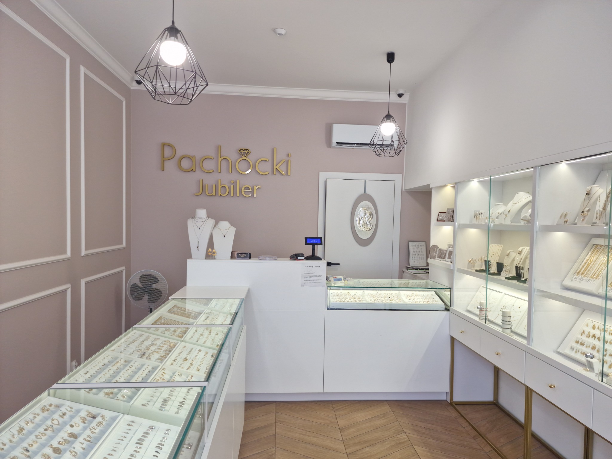 Wnętrze eleganckiego salonu jubilerskiego z przeszklonymi gablotami pełnymi biżuterii, minimalistycznym oświetleniem i klimatyzacją ścienną nad ladą.