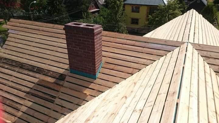 Widok z góry na konstrukcję drewnianą dachu z kominem z cegły, przygotowaną pod dalsze prace wykończeniowe.