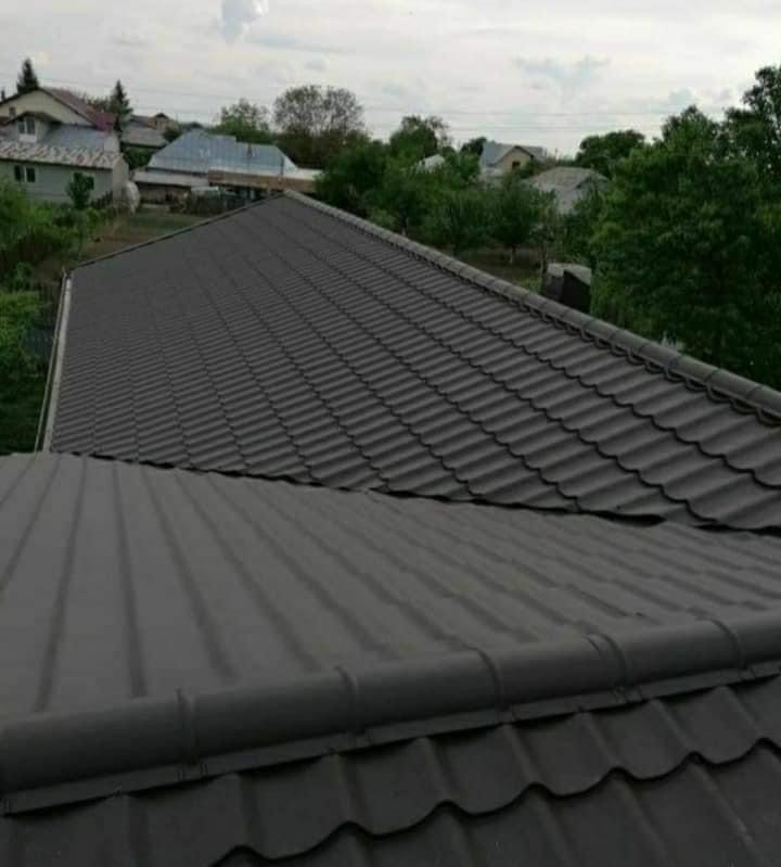 Nowy, ciemnoszary dach z blachy trapezowej, widok z góry na tle zabudowy jednorodzinnej i drzew.