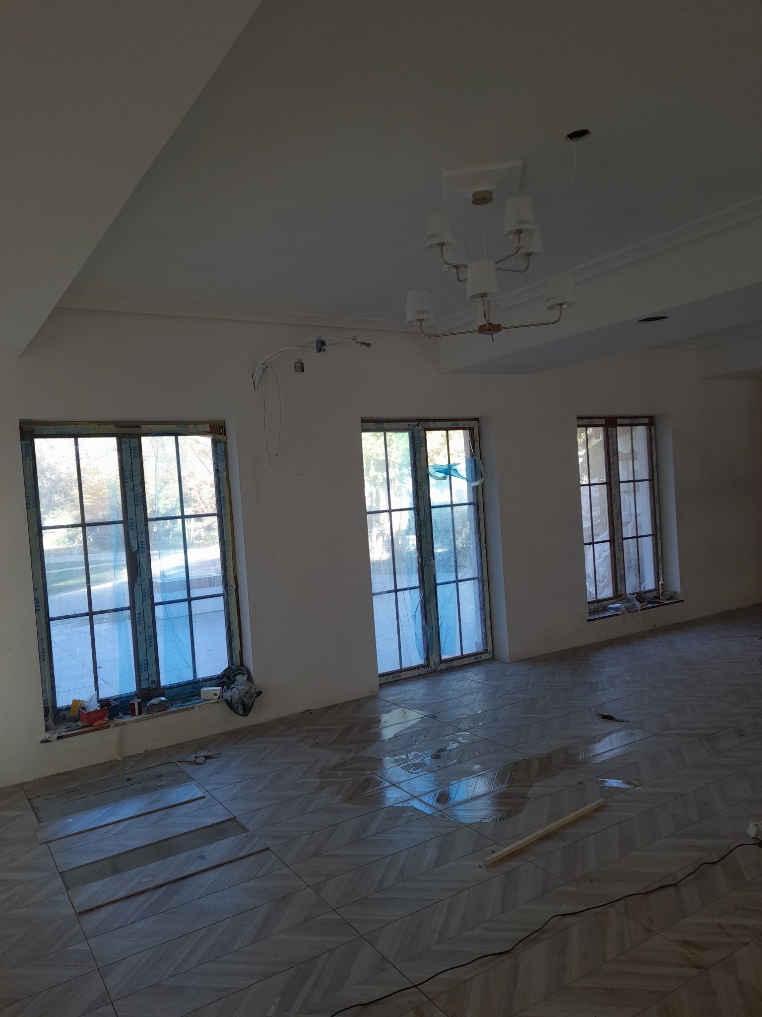 Wnętrze w trakcie układania parkietu w jodełkę, okna zabezpieczone folią, widoczne niedociągnięcia w malowaniu ścian i sufitu oraz instalacja elektryczna.