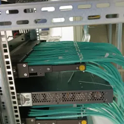 Szczegółowe ujęcie z Ostrołęki przedstawiające uporządkowane kable światłowodowe, spięte białymi opaskami zaciskowymi, w szafie rack serwerowni z widocznymi elementami wentylacyjnymi.