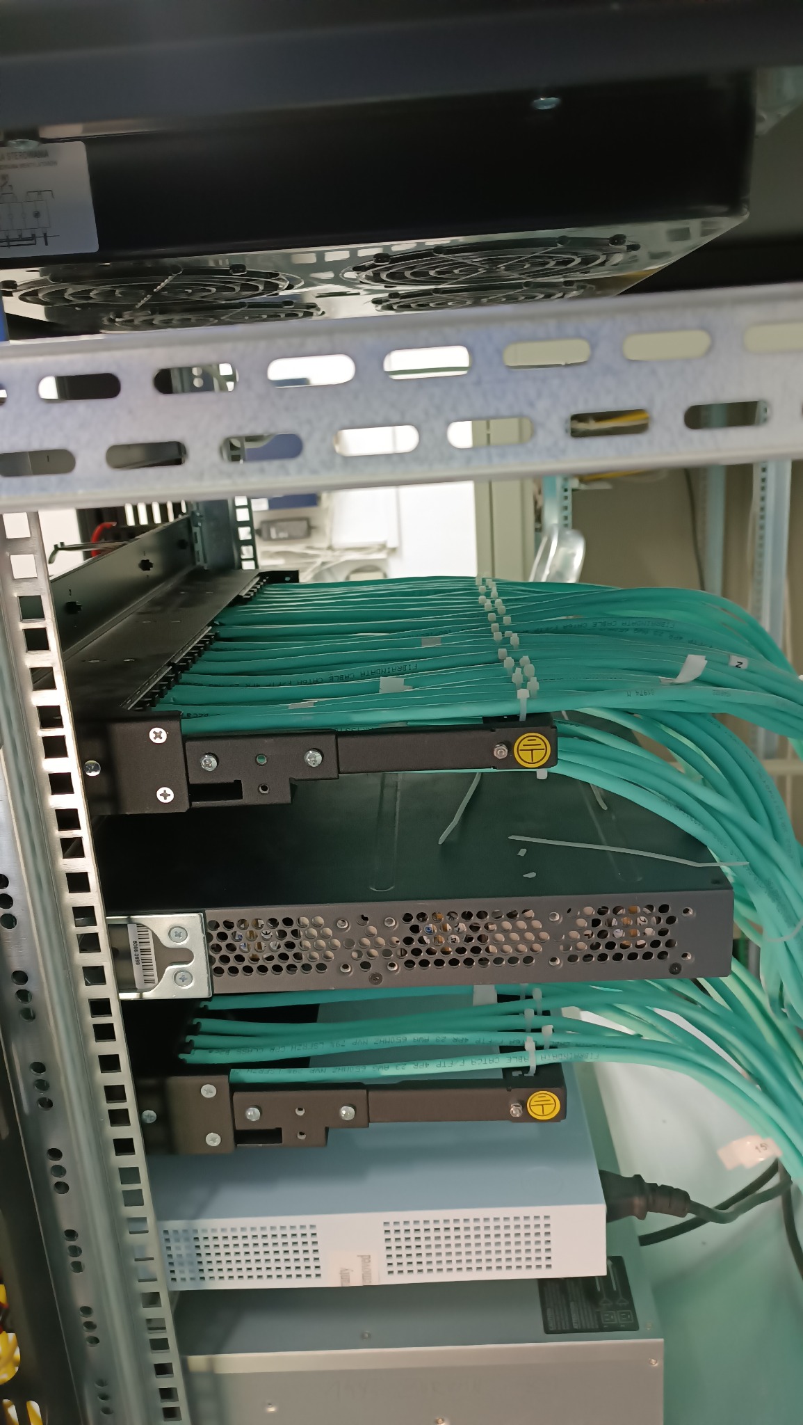 Szczegółowe ujęcie z Ostrołęki przedstawiające uporządkowane kable światłowodowe, spięte białymi opaskami zaciskowymi, w szafie rack serwerowni z widocznymi elementami wentylacyjnymi.