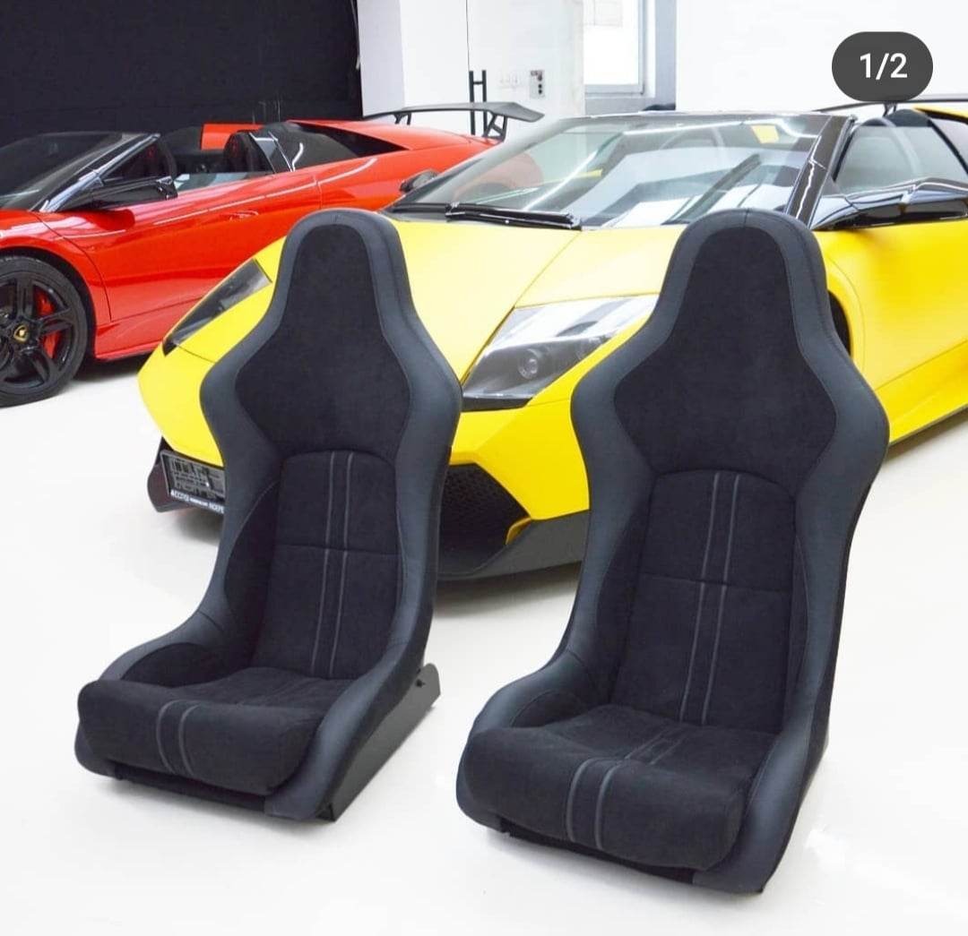 Dwa czarne, kubełkowe fotele samochodowe z szarą lamówką i przeszyciami, na tle żółtego i czerwonego sportowego samochodu w garażu.