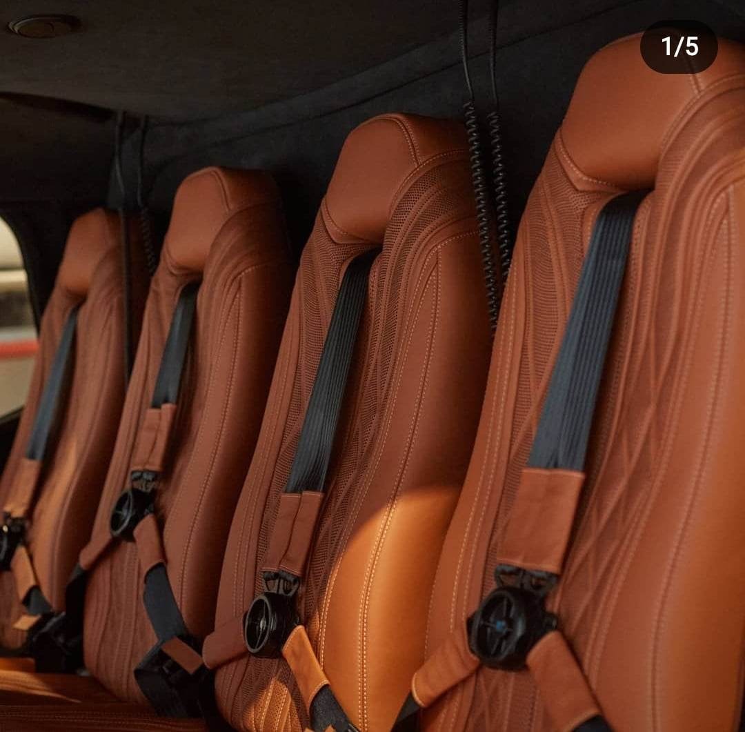 Rząd czterech skórzanych foteli w helikopterze, brązowa tapicerka z czarnymi pasami bezpieczeństwa, widoczne detale szwów i mocowań.