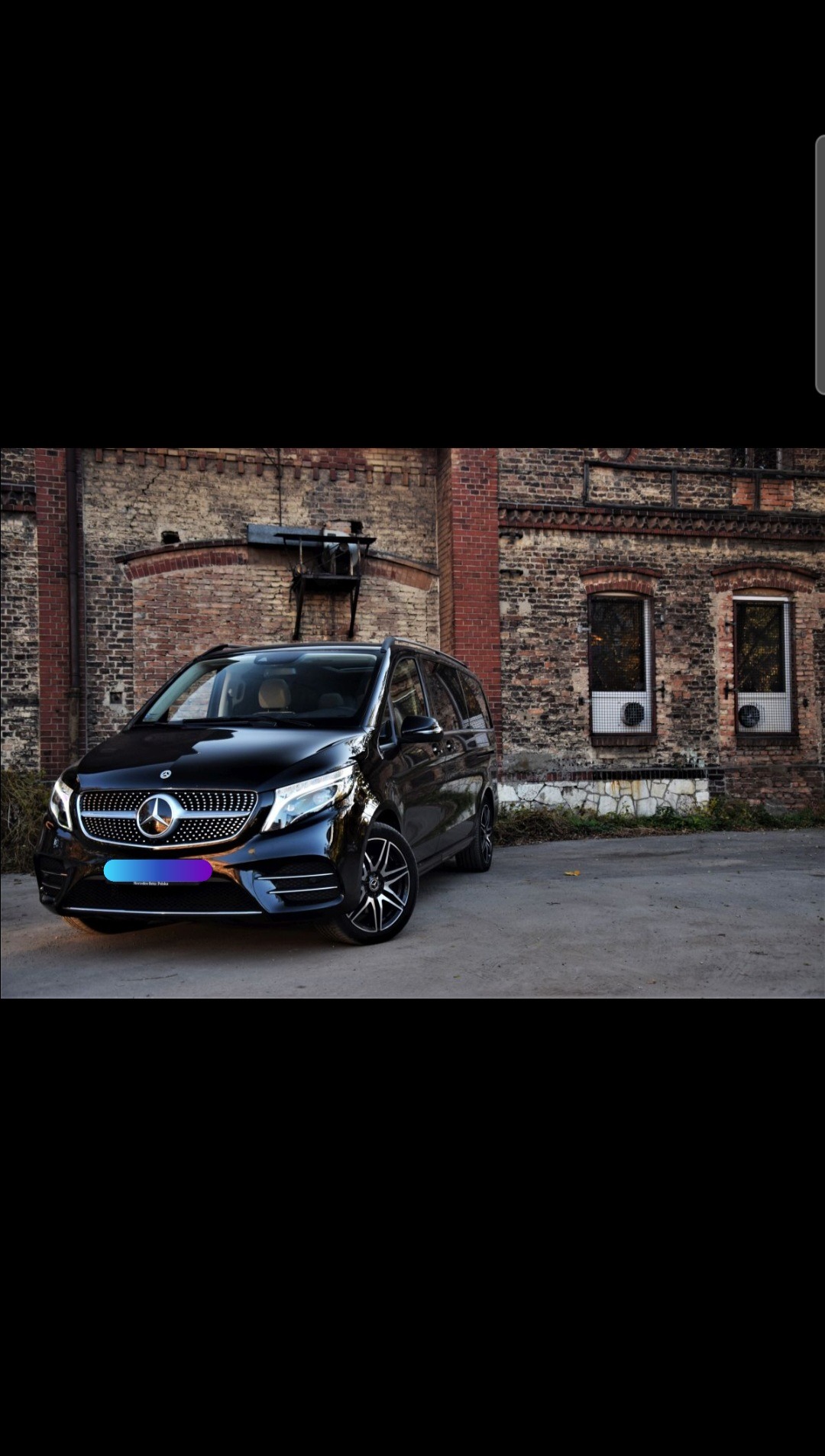 Czarny Mercedes V-klasa zaparkowany przed ceglanym budynkiem z dwoma oknami.
