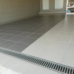 Wykończona podłoga w garażu lub pomieszczeniu gospodarczym z dwukolorową szarą i beżową glazurą oraz odpływem liniowym.