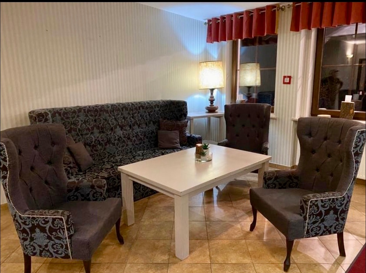 Umeblowane wnętrze pokoju z tapicerowaną sofą, dwoma fotelami typu uszak, białym stolikiem kawowym i lampami stołowymi w tle.