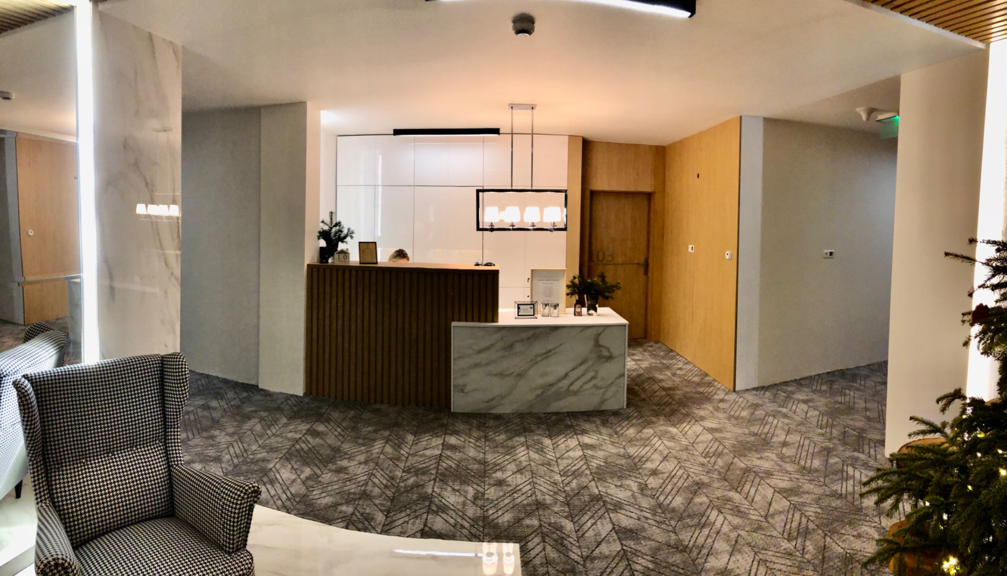 Nowoczesne wnętrze recepcji z drewnianą ladą, marmurowym wykończeniem, wzorzystą wykładziną podłogową i krzesłem w pepitkę, oświetlone wiszącą lampą.