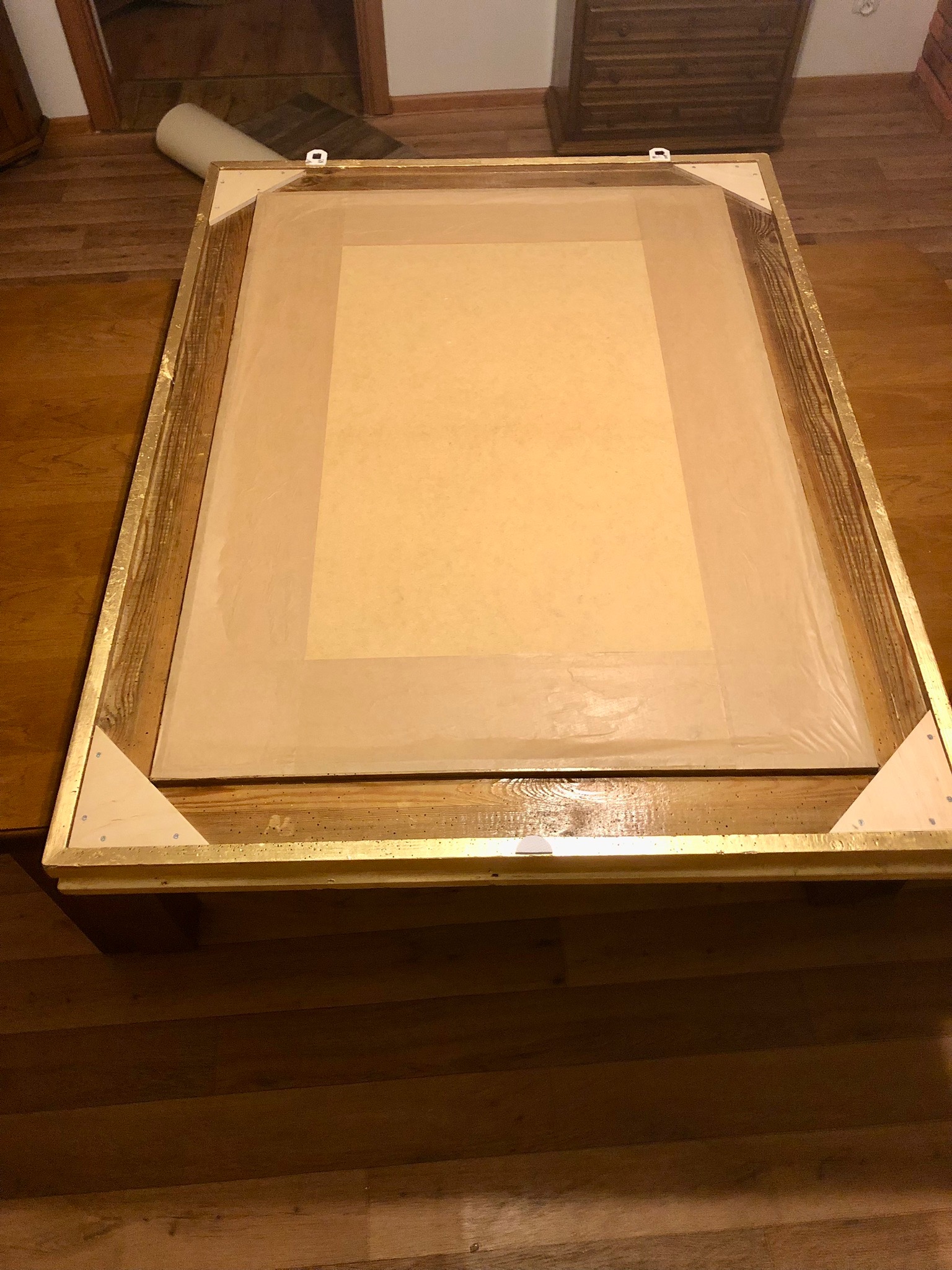 Przygotowany do malowania fragment ściany w Źlinicach, z widoczną drewnianą ramą, zabezpieczoną folią i narożnikami, leżącą na podłodze.