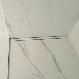 Usługi Kafelkarskie - Białe płytki imitujące marmur z odpływem liniowym w kabinie prysznicowej. Minimalistyczny design, precyzyjne ułożenie płytek, widoczny detal odpływu.