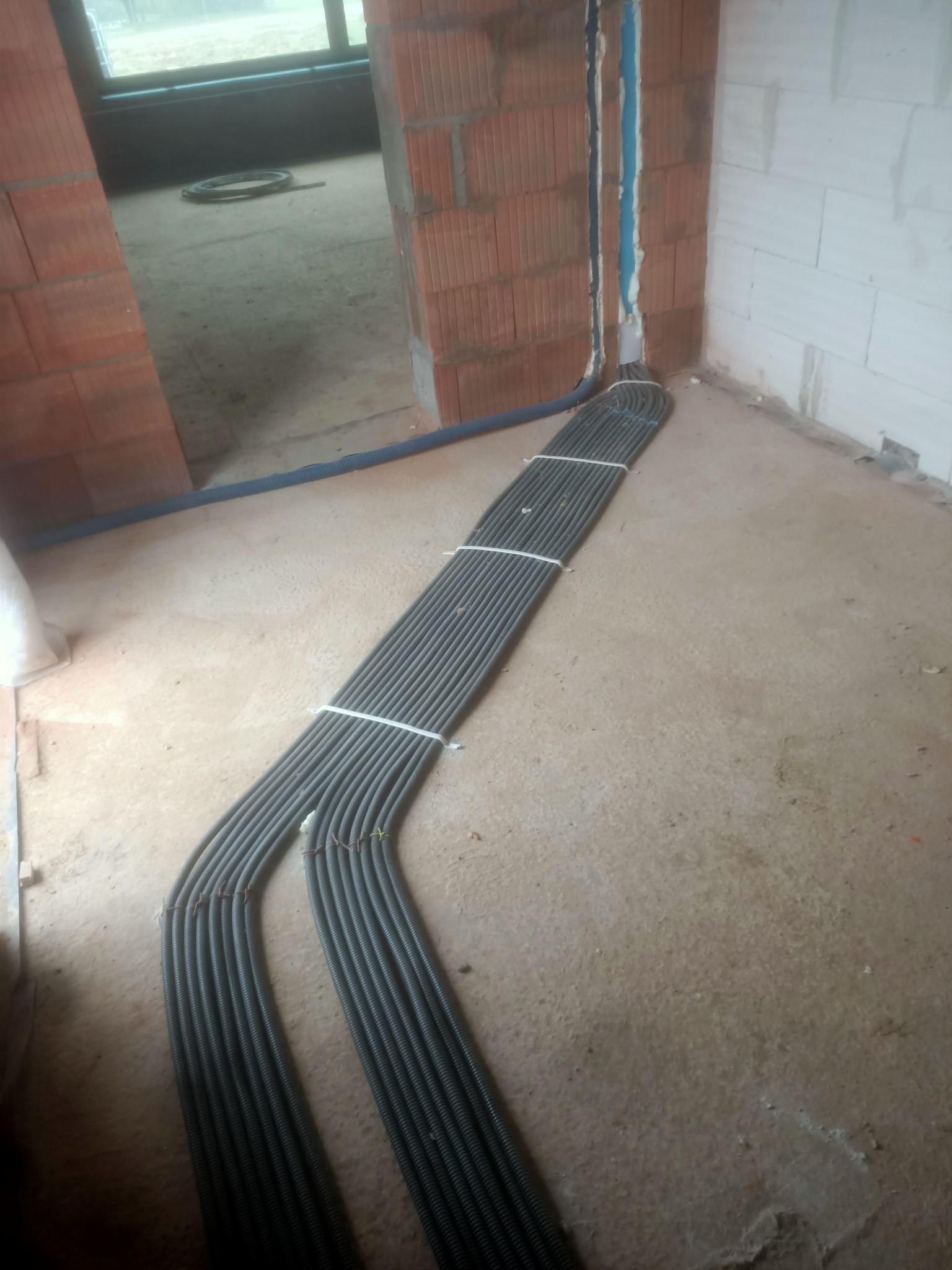 Wiązka przewodów elektrycznych w peszlach, zabezpieczona opaskami, ułożona na podłodze w trakcie prac instalacyjnych w Puławach. Widoczne bruzdy w ścianie przygotowane pod instalację.